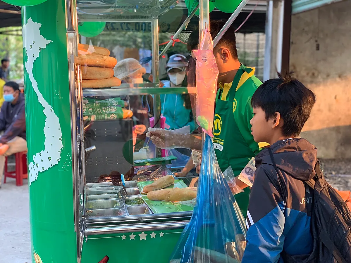 Nhân viên chuẩn bị bánh mì tại quầy có khay nguyên liệu và kệ bánh