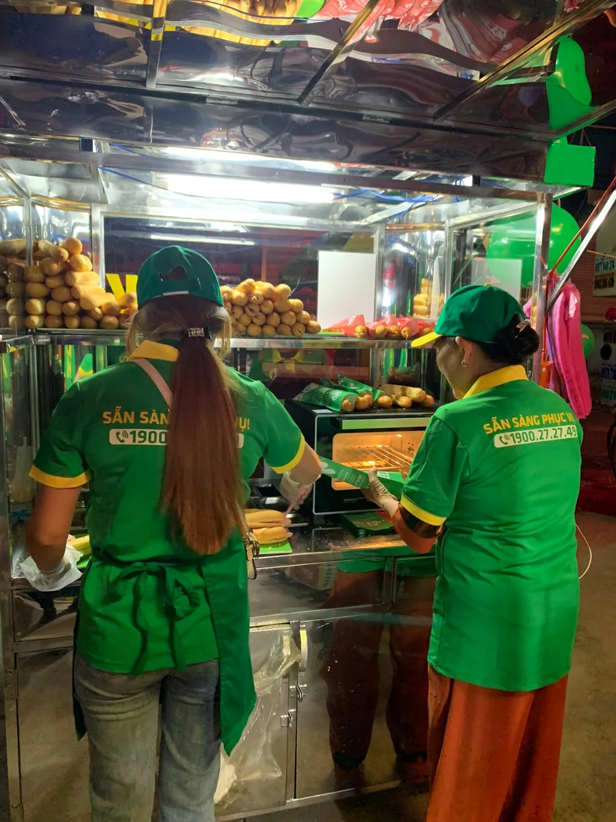 Hai người cùng chuẩn bị và làm nóng bánh mì tại một quầy bán