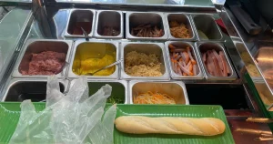 Quầy bán bánh mì với các khay nguyên liệu, dụng cụ và ổ bánh mì