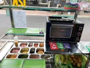 Lò nướng bánh mì cạnh các khay nguyên liệu và bánh mì tại quầy bán